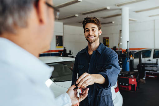 Car mechanic passing car keys to the car owner after repairing his vehicle. Mechanic giving car key to customer after servicing at garage.