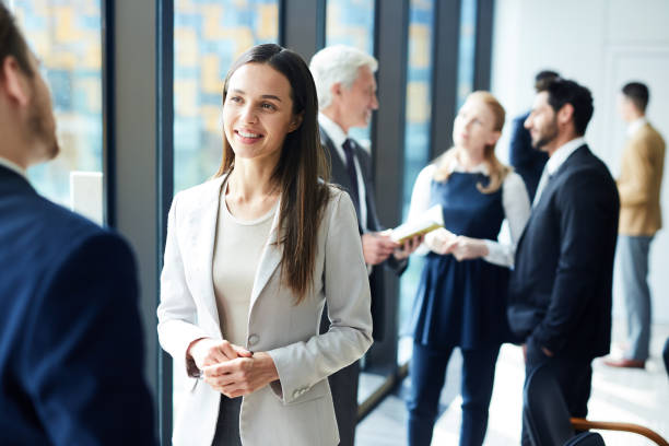 Pretty business lady talking to colleague Smiling pretty young business lady in jacket talking to colleague and discussing business forum topics during break summit meeting photos stock pictures, royalty-free photos & images