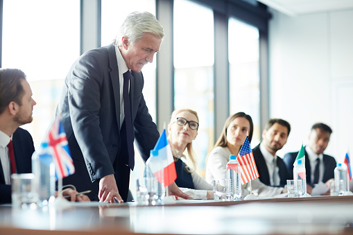 Business meeting in a luxury restaurant. Group of multi ethnic and diverse age range people attending to a corporate briefing sitting at a table after lunch.