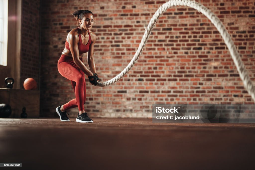 Woman doing cross training routine Woman using training rope for exercise at gym. Athlete working out with battle rope at cross training gym. Exercising Stock Photo