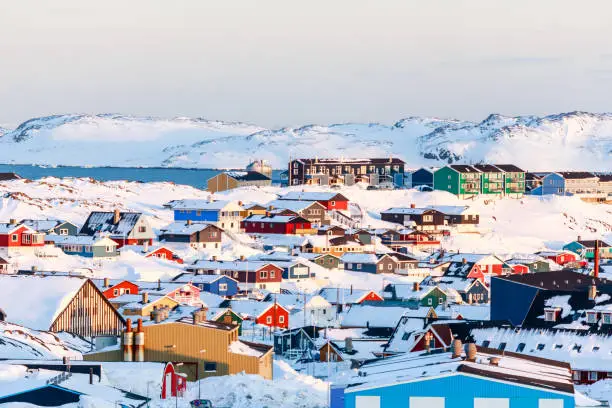 Lots of Inuit houses scattered on the hill in Nuuk city covered in snow with sea and mountains in the background, Greenland