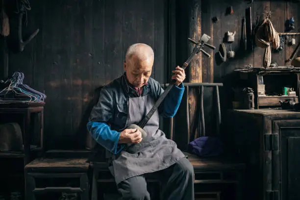 chinese senior man playing longneck lute in wooden house in daxu ancient town