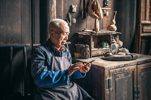sceptic looking chinese senior man tapping on mobile in old wooden house