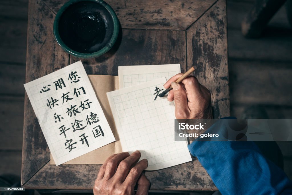 chinese senior man writing chinese calligraphy characters on paper close up of old hands writing chinese calligraphy characters with india ink on paper Mandarin Chinese Stock Photo