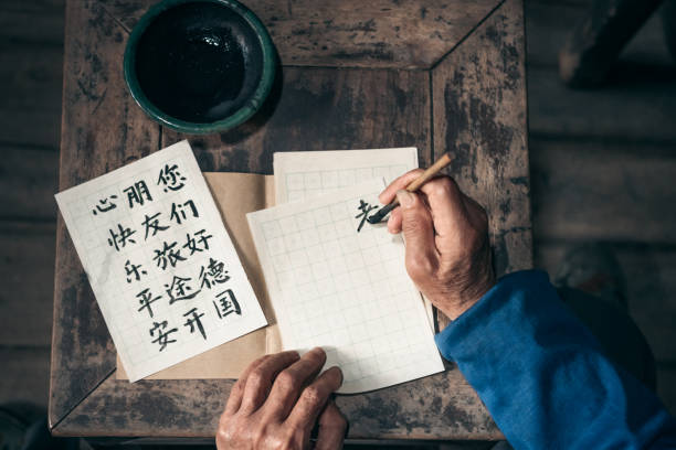 chinese senior man writing chinese calligraphy characters on paper close up of old hands writing chinese calligraphy characters with india ink on paper chinese language stock pictures, royalty-free photos & images