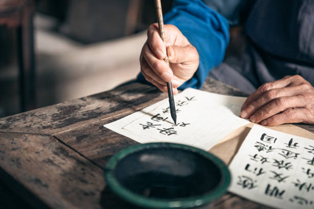hombre senior chino escribir caracteres de caligrafía china en el papel - escritura china fotografías e imágenes de stock