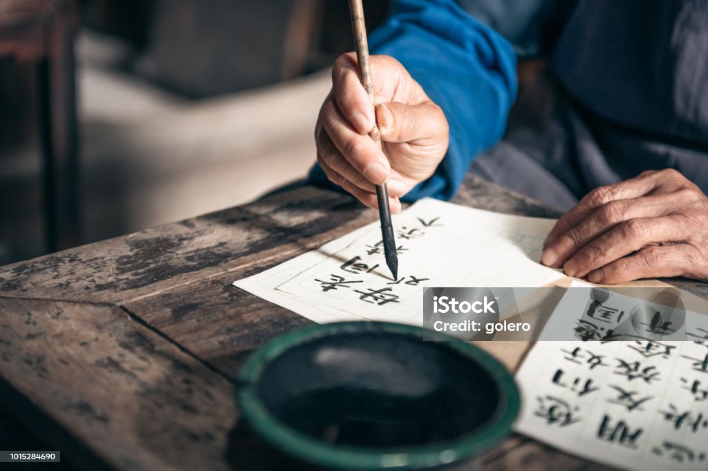 chinese senior man writing chinese calligraphy characters on paper close up of old hands writing chinese calligraphy characters with india ink on paper Chinese Script Stock Photo