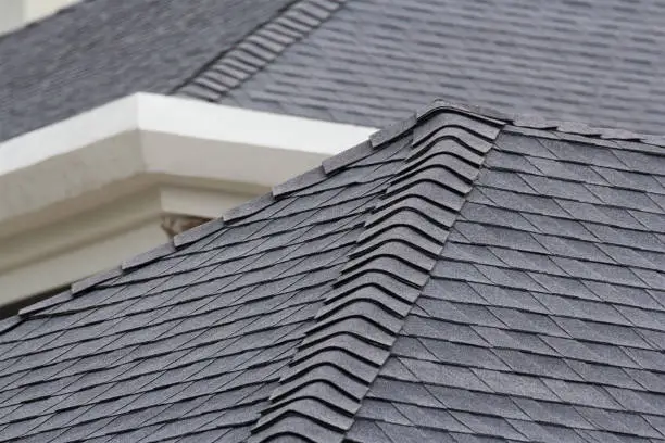 Photo of edge of Roof shingles on top of the house, dark asphalt tiles on the roof background.