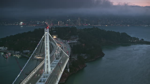 AERIAL San Francisco-Oakland Bay Bridge and the Yerba Buena Island at dusk overlooking the city of San Francisco