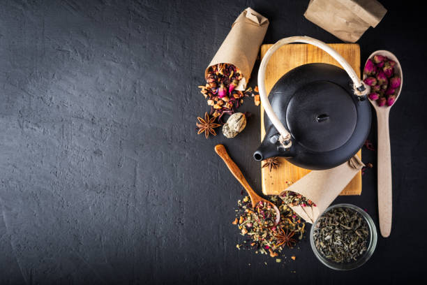 istock Black ceramic teapot with tea, Different tea and herbs , dried rose flowers on dark concrete background. Top view, copy space. 1015304528