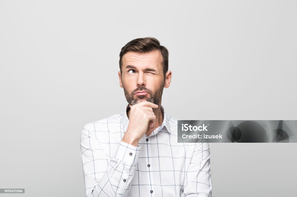 Portrait of pensive businessman, grey background Portrait of handsome successful businessman wearing white shirt, thinking with hand on chin against grey background. Studio shot. Asking Stock Photo