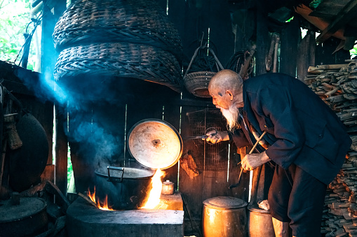 old chinese senior man cooking water in simple kitchen