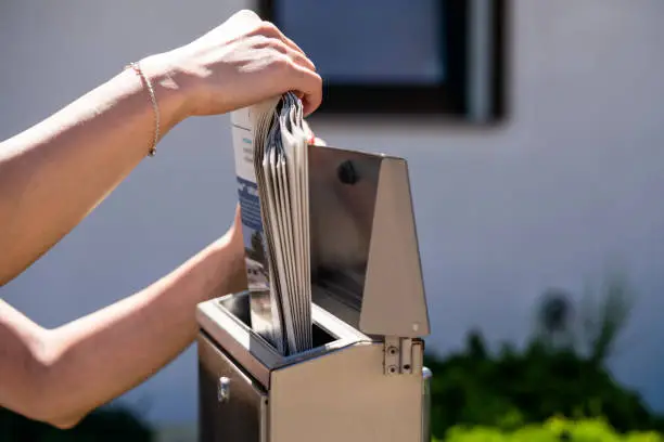 A woman takes a newspaper off a mailbox.