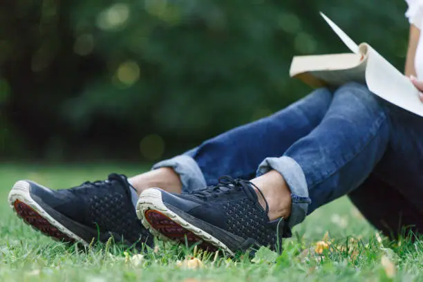Concept - relax in the park. On a grass background, in the background a girl reads a book. A woman in blue jeans in a soft focus.