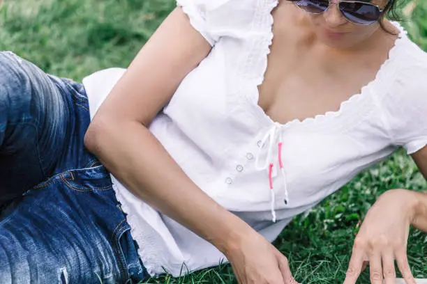 Portrait of middle-aged brunette woman. In sunglasses the girl lies on the grass in the park and reads the book.