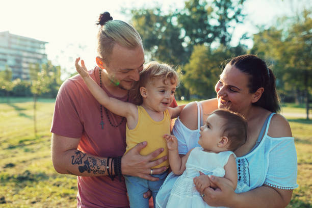 Modern real parents with body positive attitude, tattoos, piercings and positive lifestyle, spending afternoon with their kids in the park.
