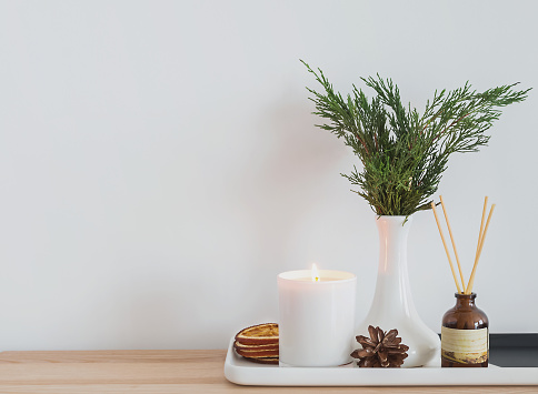 Cozy modern home details. Burning candle, aroma sticks and other elements in the small table near the white wall.