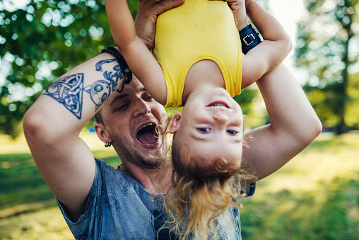 Modern real parents with body positive attitude, tattoos, piercings and positive lifestyle, spending afternoon with their kids in the park.