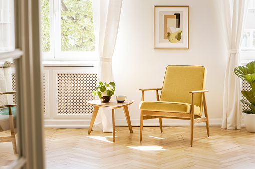 Un retro, amarillo sillón y una mesa de madera en un interior hermoso, soleado living comedor con piso y blanca paredes de espina de pescado. Foto real. photo