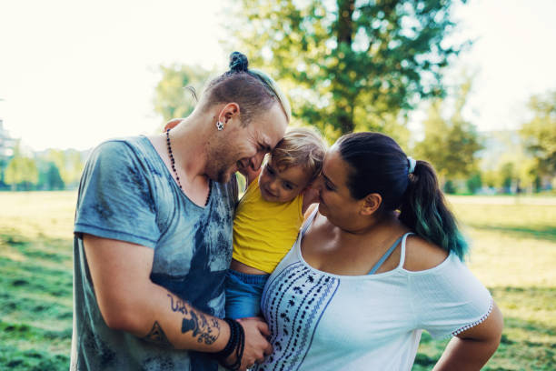 Modern real parents with body positive attitude, tattoos, piercings and positive lifestyle, spending afternoon with their kids in the park.