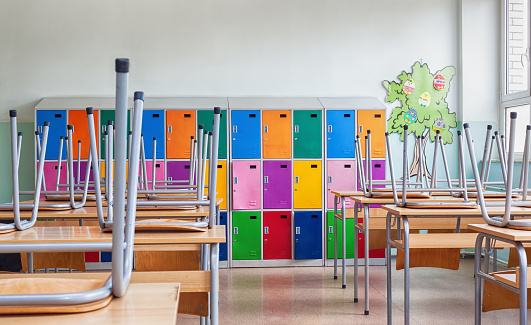 Modern emty classroom with colorful lockers and raised chairs on the tables