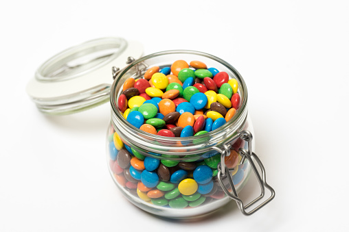 Clip top jar full of colourful sugar-coated candies on a white bakground