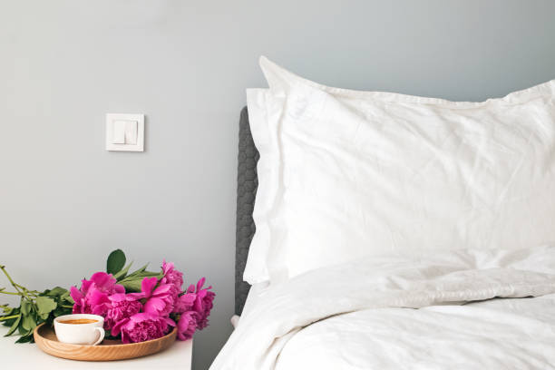 istock Bed with white bed sheets and pink peonies and coffee on the nightstand. 1015370600
