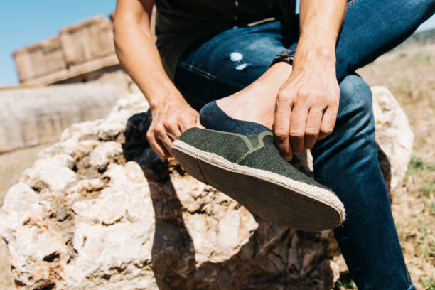 young man putting on or taking off his shoe closeup of a young caucasian man sitting on a rock outdoors putting on or taking off his shoe, with a low cut sock on his foot cleavage stock pictures, royalty-free photos & images