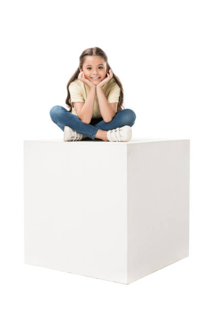 istock smiling child in casual clothing sitting on white cube isolated on white 1015371172