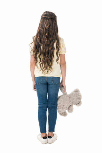 back view of little kid with teddy bear in hand standing isolated on white