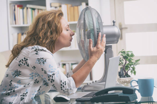 Woman suffers from heat in the office or at home Woman suffers from heat while working in the office and tries to cool off by the fan hot women working out pictures stock pictures, royalty-free photos & images