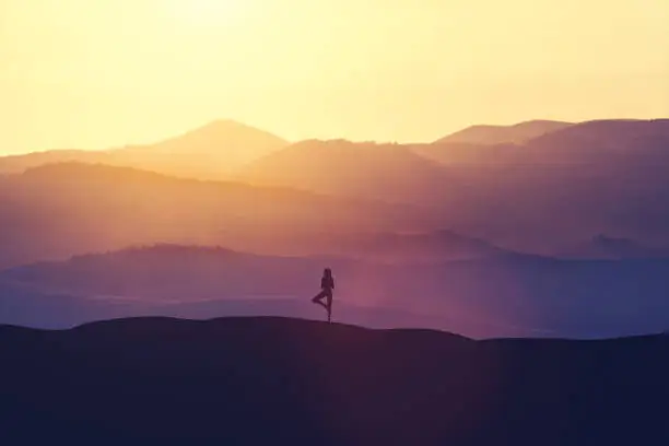 Photo of Woman standing on the hill, practicing yoga.