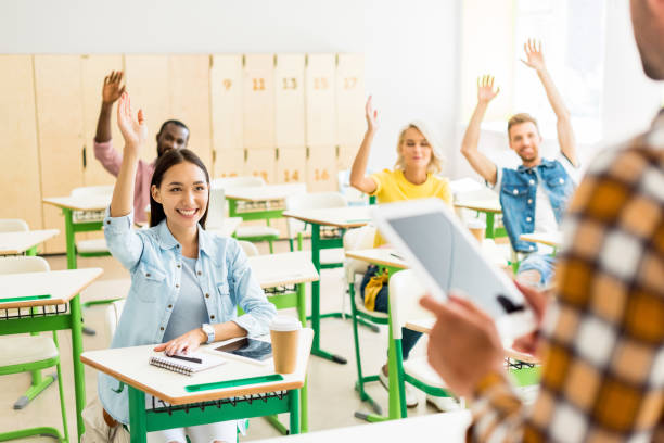 istock young students raising up hands to answer on teachers question while he standing with tablet on foreground 1015393342