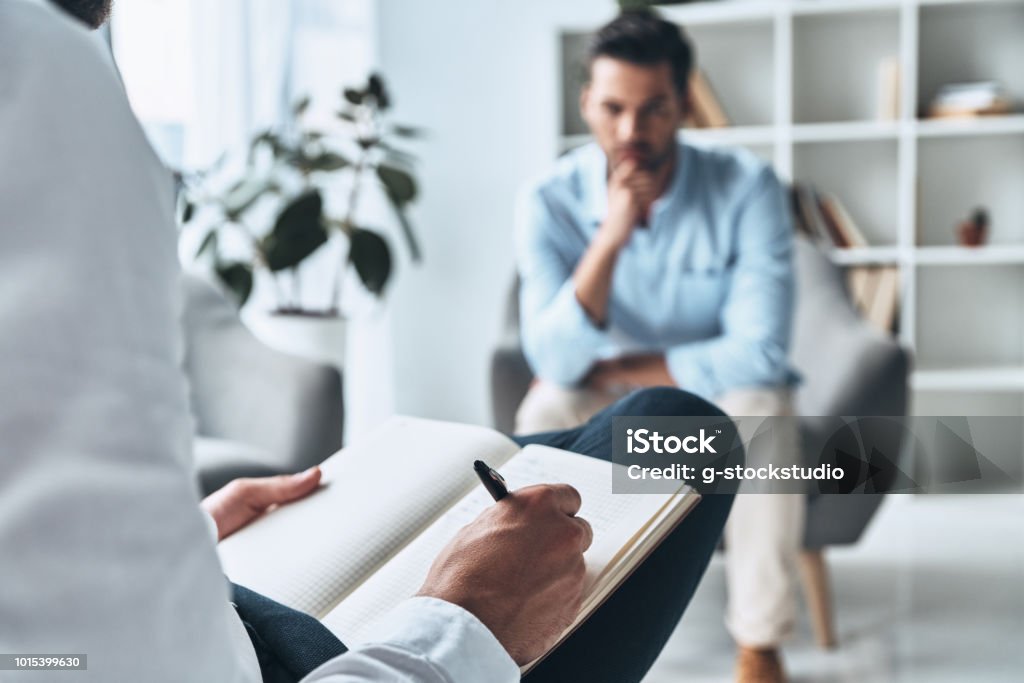 Making profile. Young frustrated man solving his mental problems while having therapy session with psychologist Mental Health Professional Stock Photo