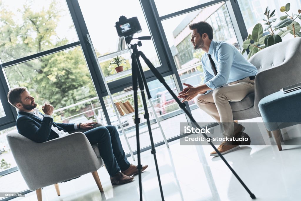 Creating interesting content. Two young men in smart casual wear talking while making new video indoors Home Video Camera Stock Photo