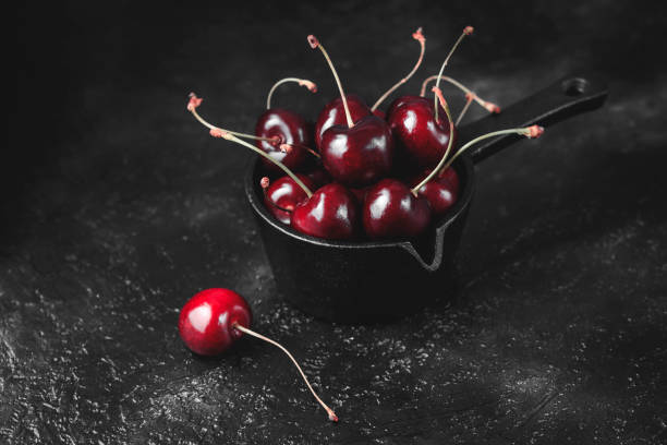 istock Fresh ruby cherries on black background. Dark moody close up still life 1015406402
