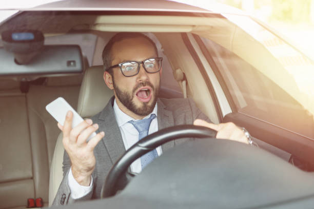 istock shocked handsome man holding smartphone and looking away in car 1015408746