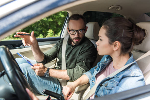 istock teacher pointing on something to student in car during driving test 1015409726