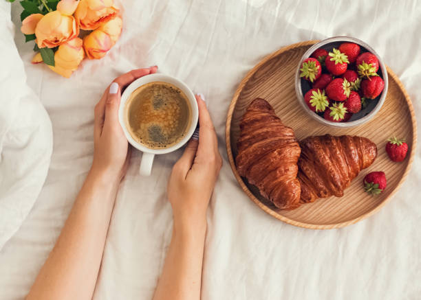 istock Woman's hands holding a cup of coffee on the bed with white bedsheet. 1015410320