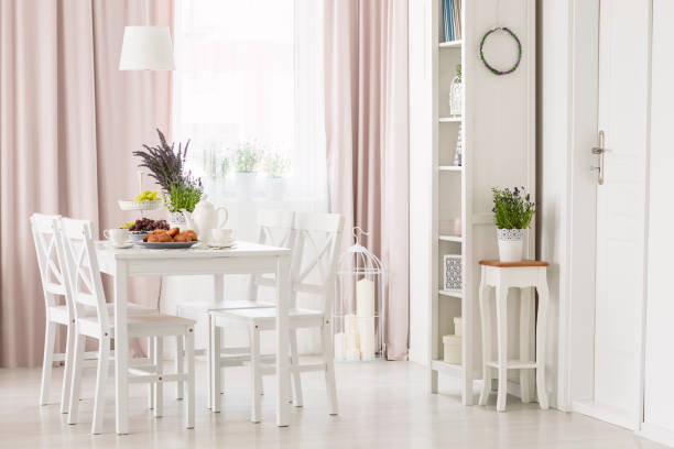istock White chairs at dining table with plants in modern flat interior with pink drapes and window. Real photo 1015430086