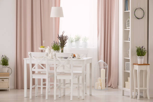 istock Lamp above table and white chairs in pink dining room interior with plants and drapes. Real photo 1015430088