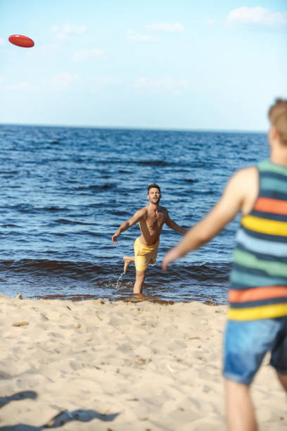 istock selective focus of young men playing with flying disc on sandy beach 1015430442