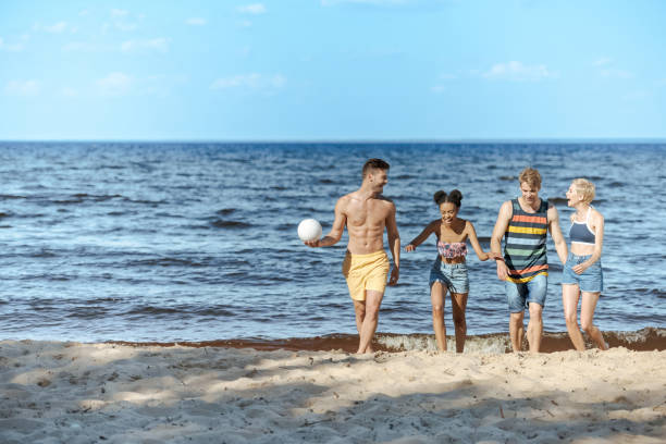 istock multicultural friends with volleyball ball walking on sandy beach 1015430486