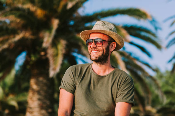 Young man standing by the palm trees looking at sun