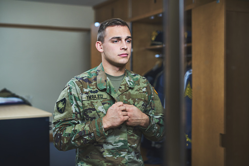 Shot of a young soldier standing getting dressed in the dorms of a military academy