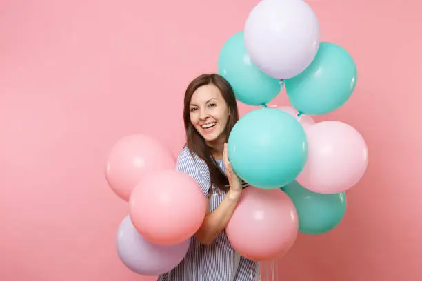 Portrait of beautiful smiling young happy woman wearing blue dress holding colorful air balloons isolated on bright trending pink background. Birthday holiday party, people sincere emotions concept
