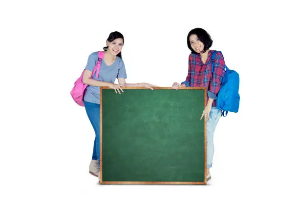 Image of two female college students holding a green board with copy space, isolated on white background