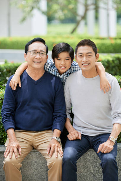 Asian boy hugging father and grandfather Cute Asian boy smiling and looking at camera while embracing cheerful father and grandfather in park vietnamese old man portrait stock pictures, royalty-free photos & images