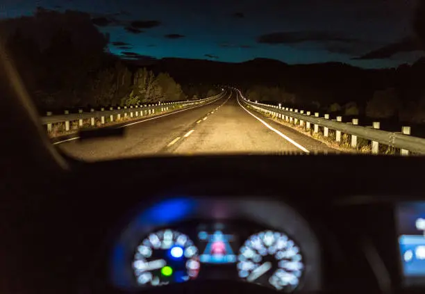 A curving country road in Utah, USA, illuminated by a car's headlights, with the car's dashboard in the foreground.