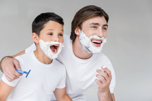 istock excited father and son with shaving foam on faces isolated on grey 1015508878